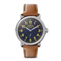 The Engravable Runwell Watch - Collegiate by Shinola features a brown leather strap, silver case, dark blue face with yellow numbers and hands, "Shinola" and "Detroit" on the dial, plus a small seconds subdial above 6 o'clock.