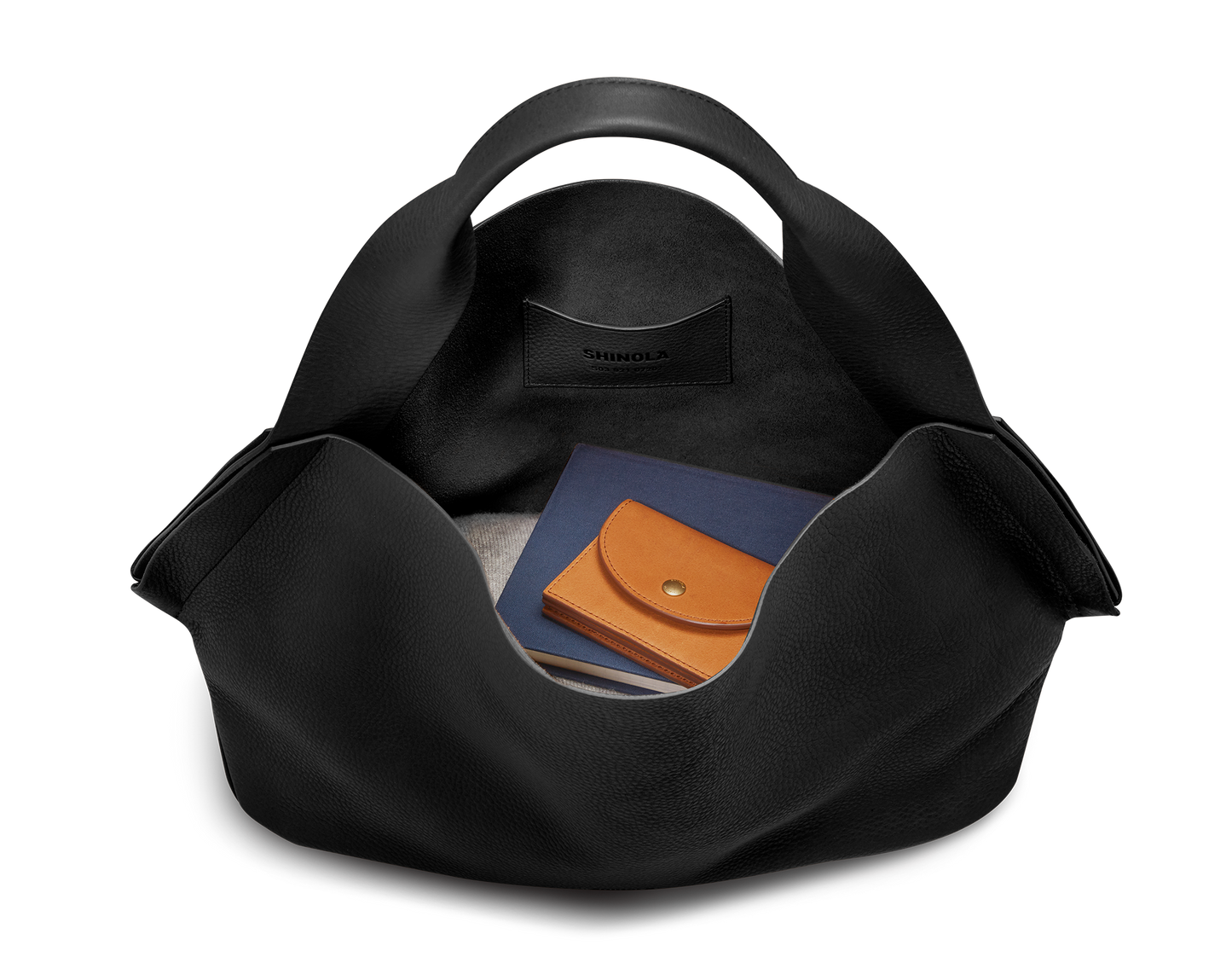 A black Derby Shoulder Bag by Shinola sits open on a plain white background, displaying a tan leather wallet and navy blue notebook inside its spacious interior with a leather card pocket stamped "Shinola.