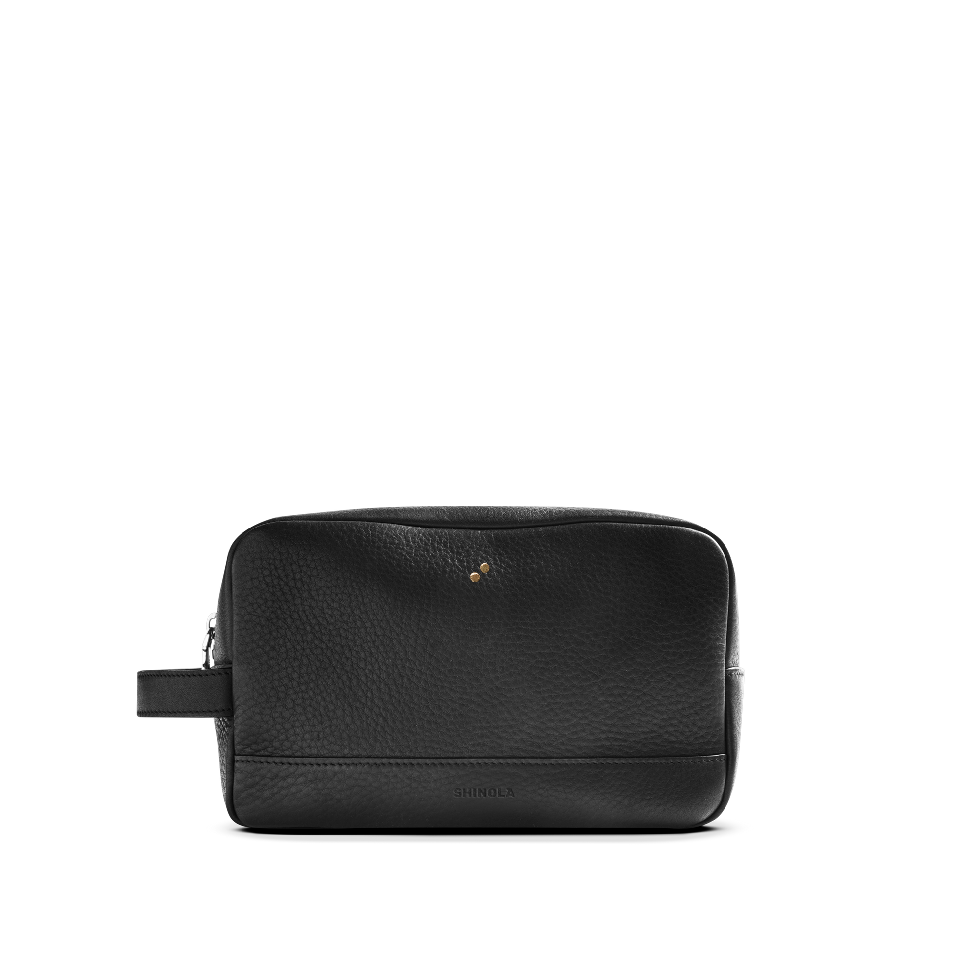 The Shinola Zip Travel Kit - Dominos is a black natural grain leather toiletry bag with a side handle, gold-tone studs, subtle embossed logo, water-resistant lining, and zip closure, shown on a plain white background.