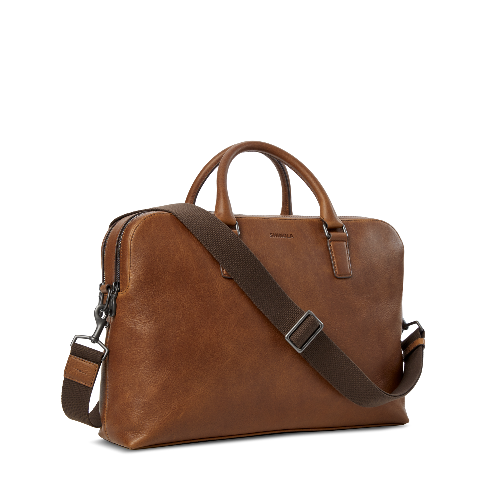 The Shinola Double Zip Briefcase in medium brown features two top handles, an adjustable shoulder strap, and is crafted from premium Navigator leather, shown here against a plain white background.