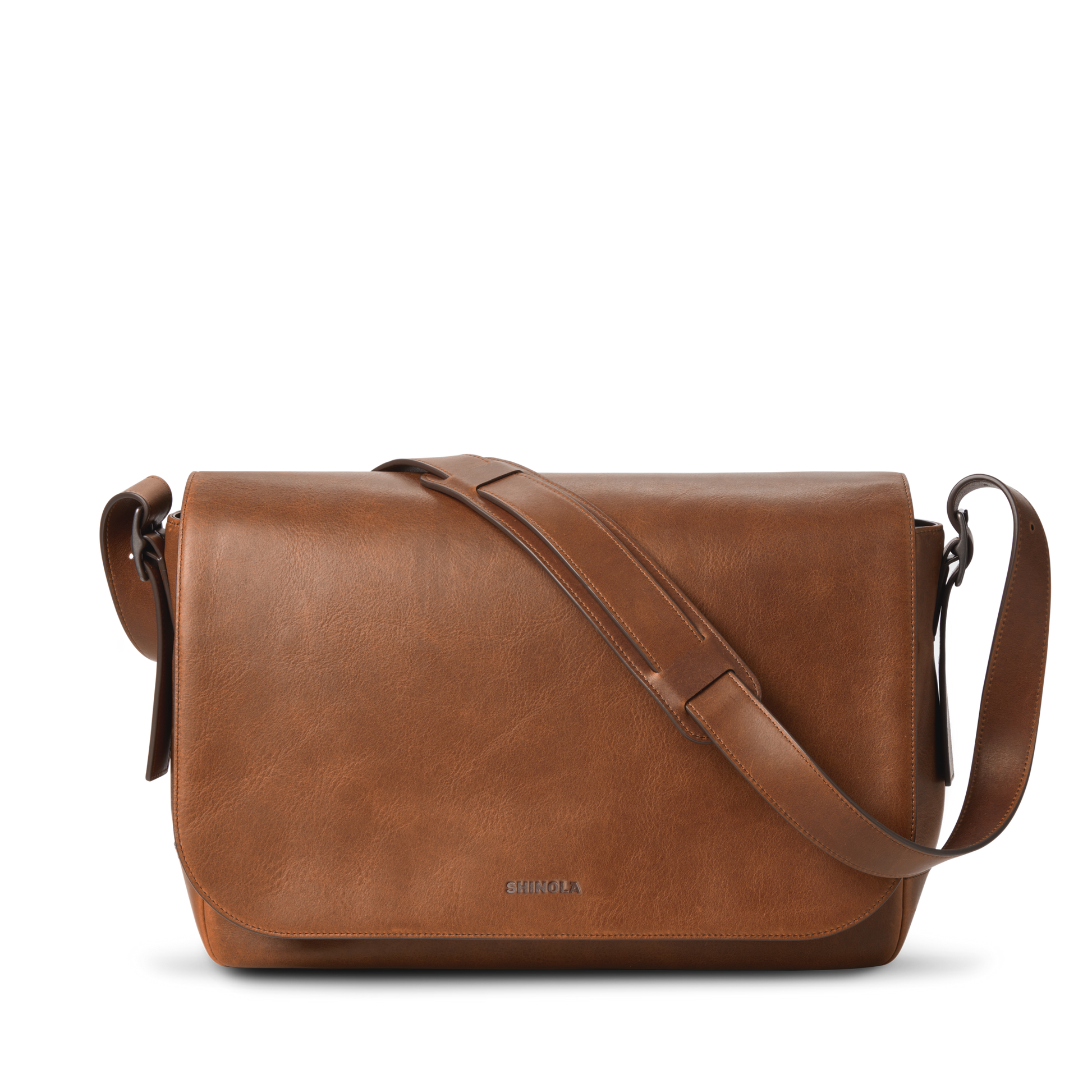 The Runwell Messenger Bag in medium brown by Shinola features a large flap closure, an adjustable crossbody strap, and the Shinola logo embossed near the bottom center. Displayed on a white background.