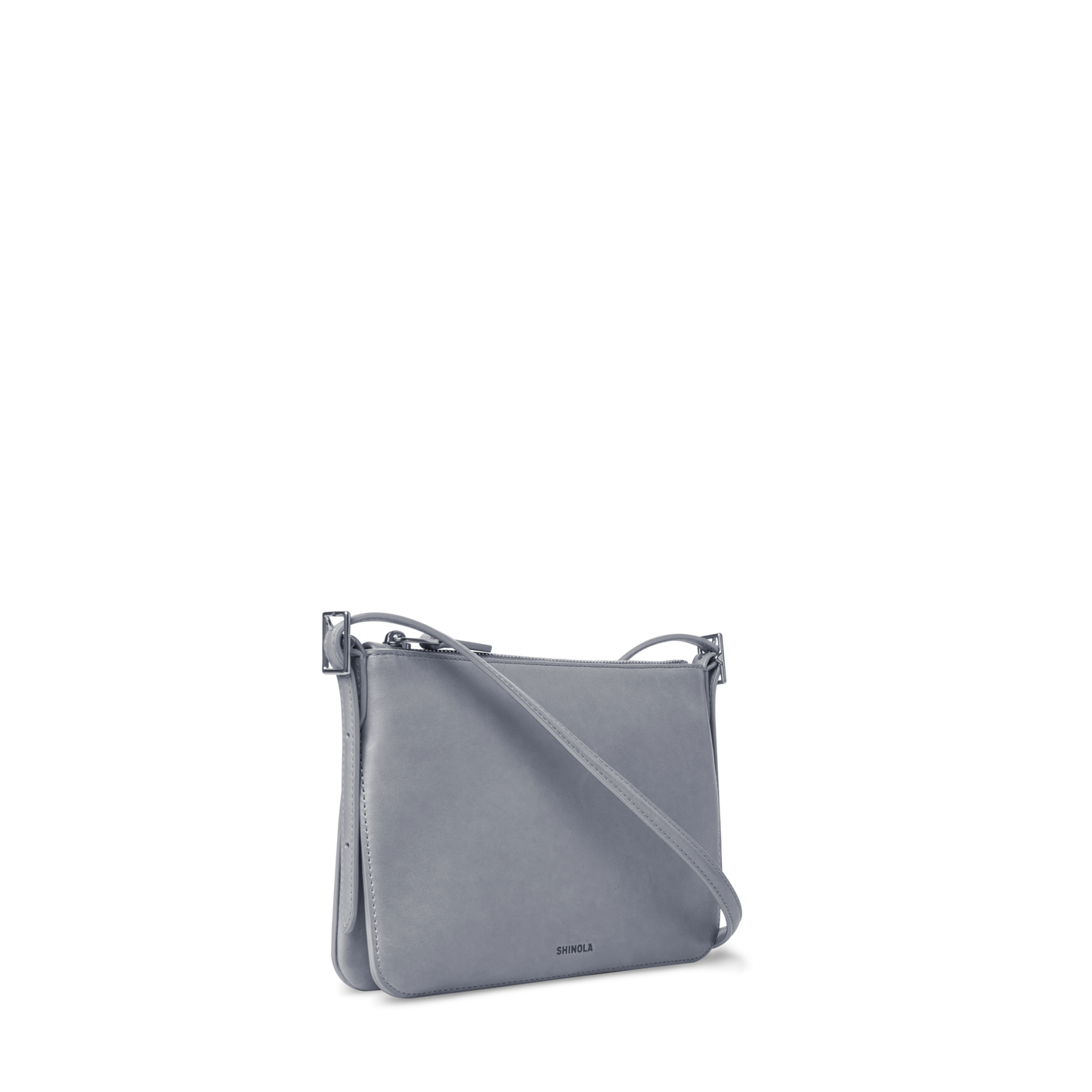 The Small Bixby Crossbody - Mist by Shinola is a light gray, rectangular bag crafted from natural leather with a slim design, long shoulder strap, subtle silver hardware, and minimalist SKYLAR logo—perfect for everyday use.