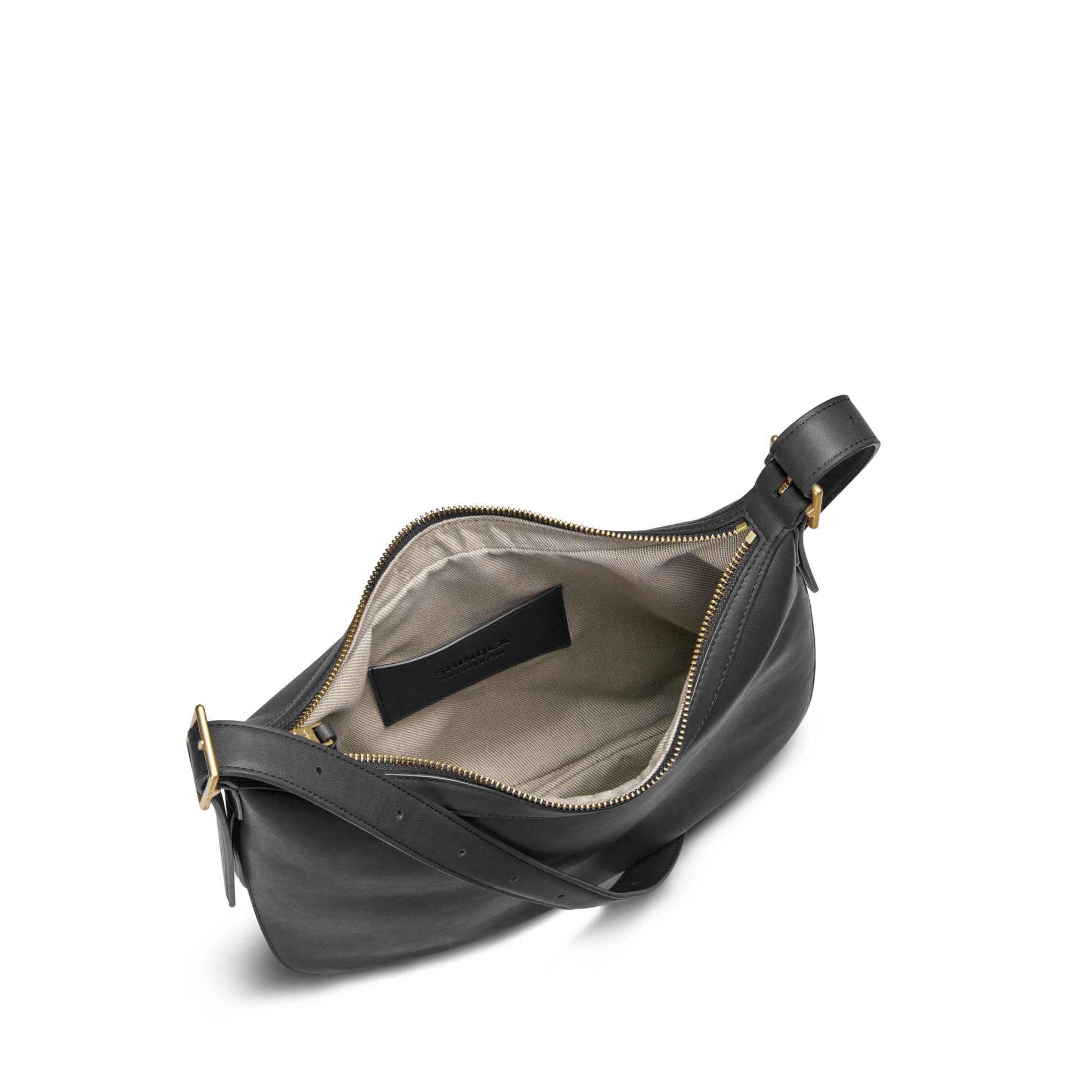 The Shinola Bixby Shoulder Bag - Black features natural leather, accordion design, gold zipper, beige fabric lining, small inner pocket, black label, and an adjustable strap with a gold buckle.