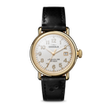 The Shinola Runwell Watch - Dominos features a gold stainless steel case, white dial with black Arabic numerals and date display, and a black leather strap, shown against a plain white background.