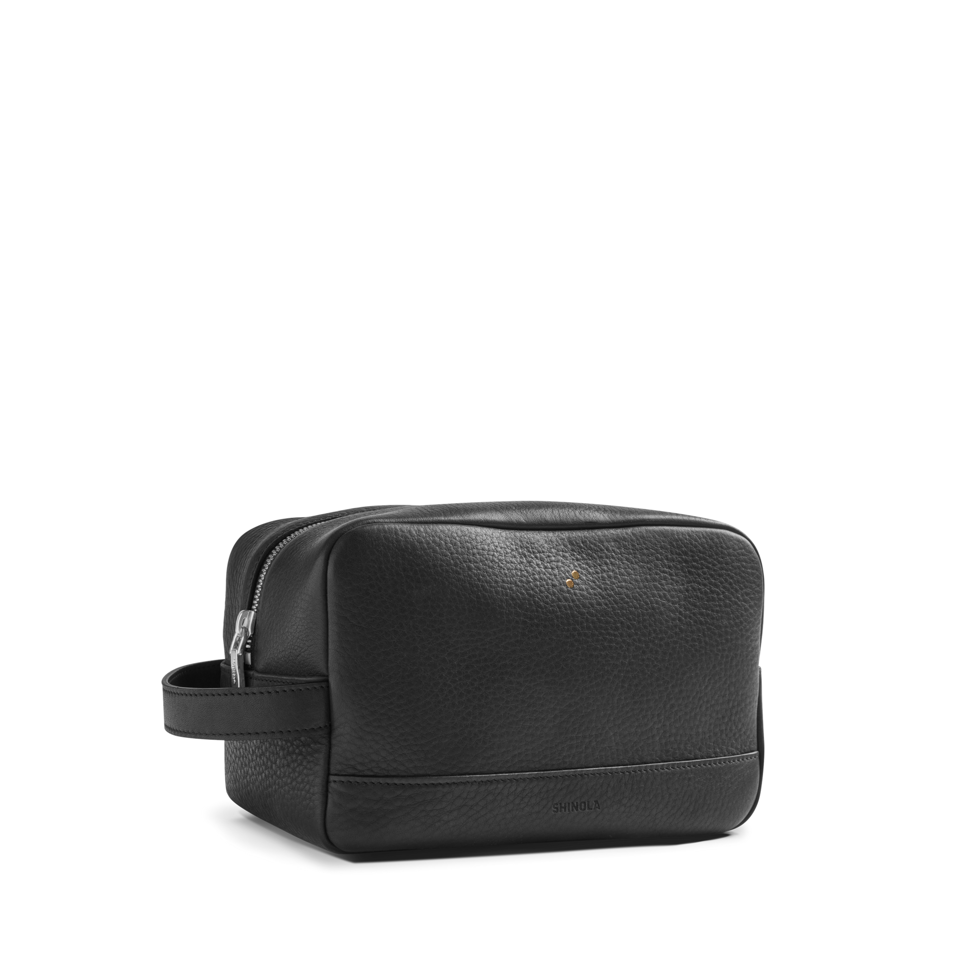 The Shinola Zip Travel Kit - Dominos features black leather with a natural grain finish, zippered top, small side handle, subtle front branding, and water-resistant lining, displayed on a plain white background.
