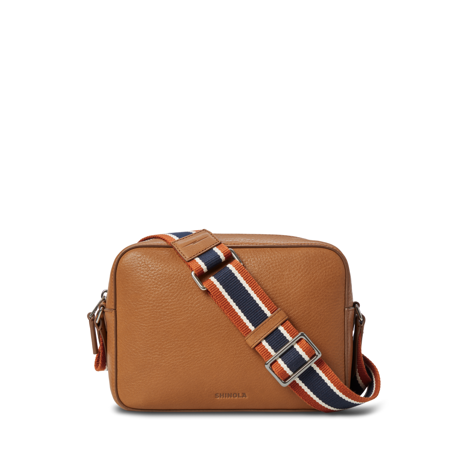 The Camera Crossbody Bag - Tan by Shinola features tan leather, a rectangular shape, silver hardware, a front flap, and an adjustable strap with orange, navy, and white stripes; "Shinola" is stamped near the bottom.