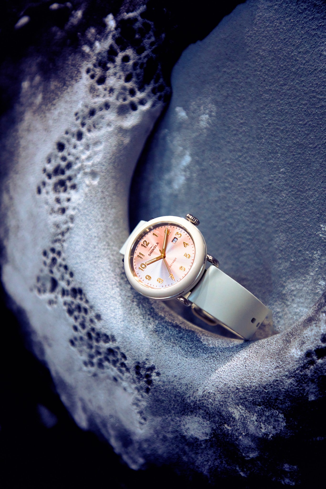 The Shinola Detrola Watch - Nude features a rose gold dial and numerals, displayed on a textured, snow-dusted surface, highlighting its classic American design and durable build against the icy backdrop.