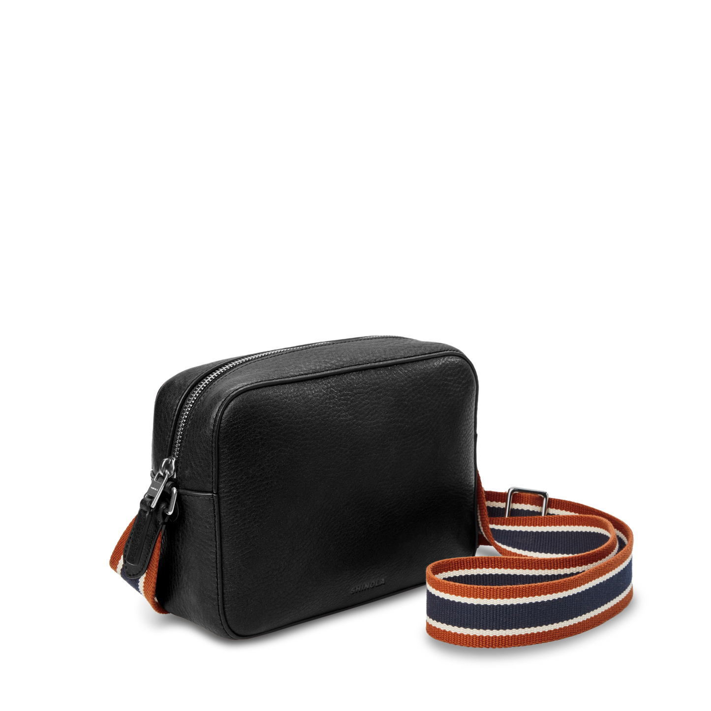 The Shinola Camera Crossbody Bag - Black is a small leather bag with a zip closure and a wide, adjustable woven strap in orange, navy blue, and white stripes—ideal for everyday use and shown against a plain white background.