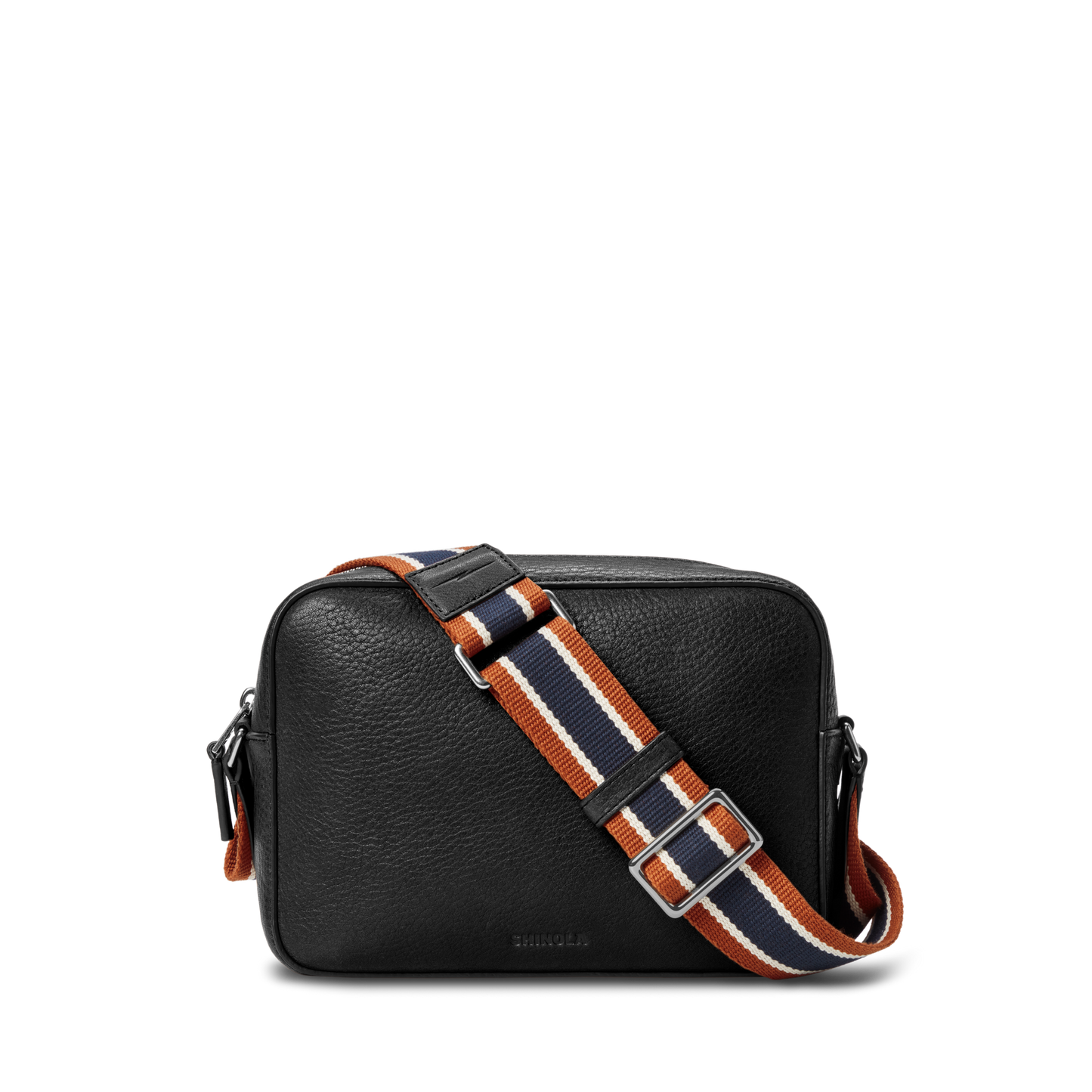 The Shinola Camera Crossbody Bag - Black is a small leather bag with a textured finish and a wide, adjustable orange, navy, and white striped woven strap, shown against a plain white background.