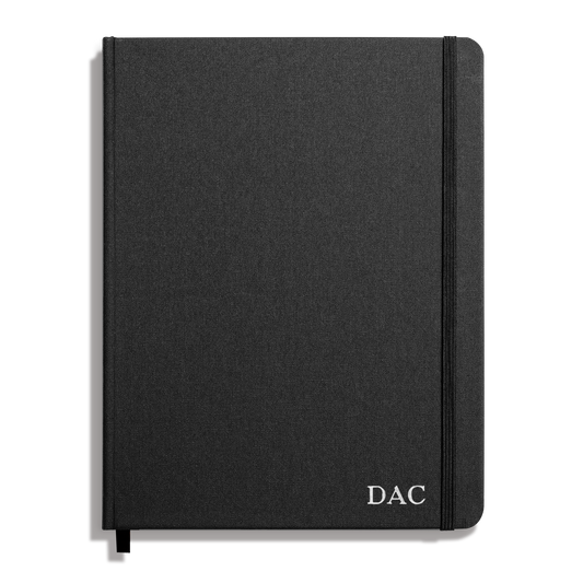 The Shinola Large Hard Ruled Journal in black features a textured cover, smyth-sewn binding, an elastic band on the right edge, and "DAC" initials printed in white on the lower right corner.