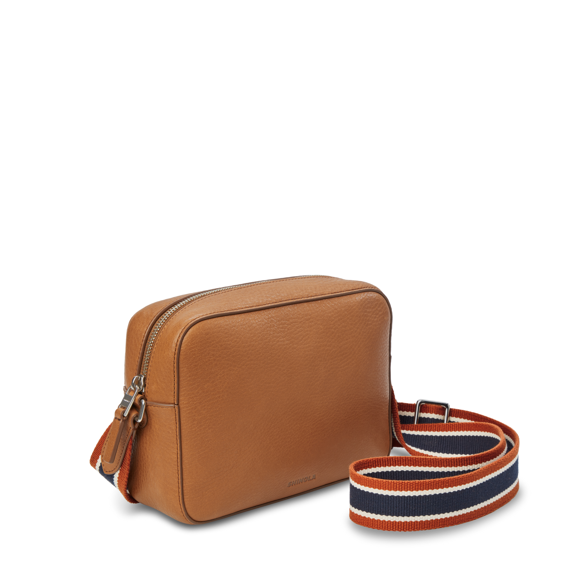 The Shinola Camera Crossbody Bag - Tan is a small leather bag with a silver zipper and an adjustable strap in orange, navy blue, and white stripes. The 35mm bag is shown on a plain white background.