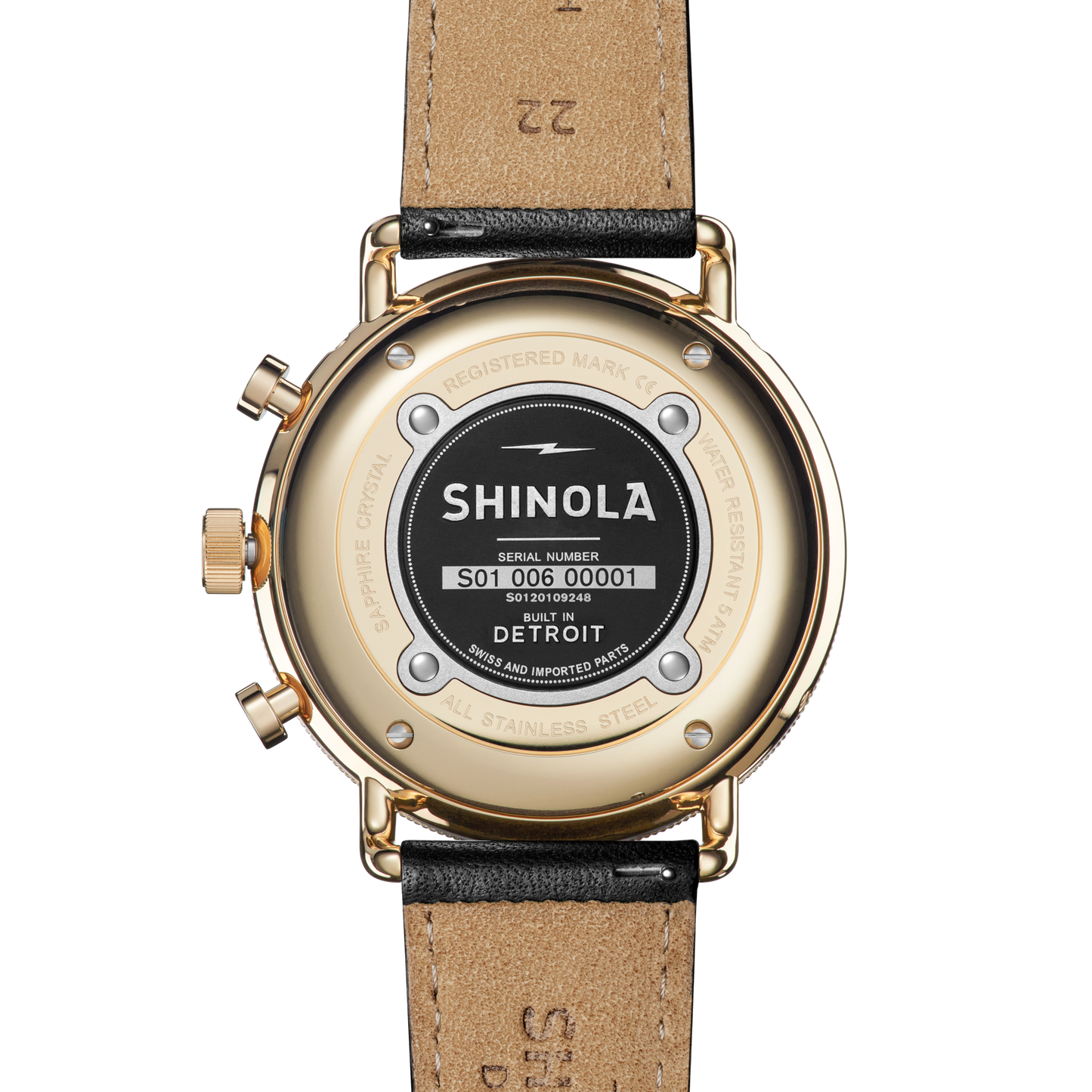 Close-up of the back of a Shinola Canfield Sport Watch - Dominos, featuring serial number, brand info, and “Built in Detroit” engraved on its gold and stainless steel case with a black leather strap.