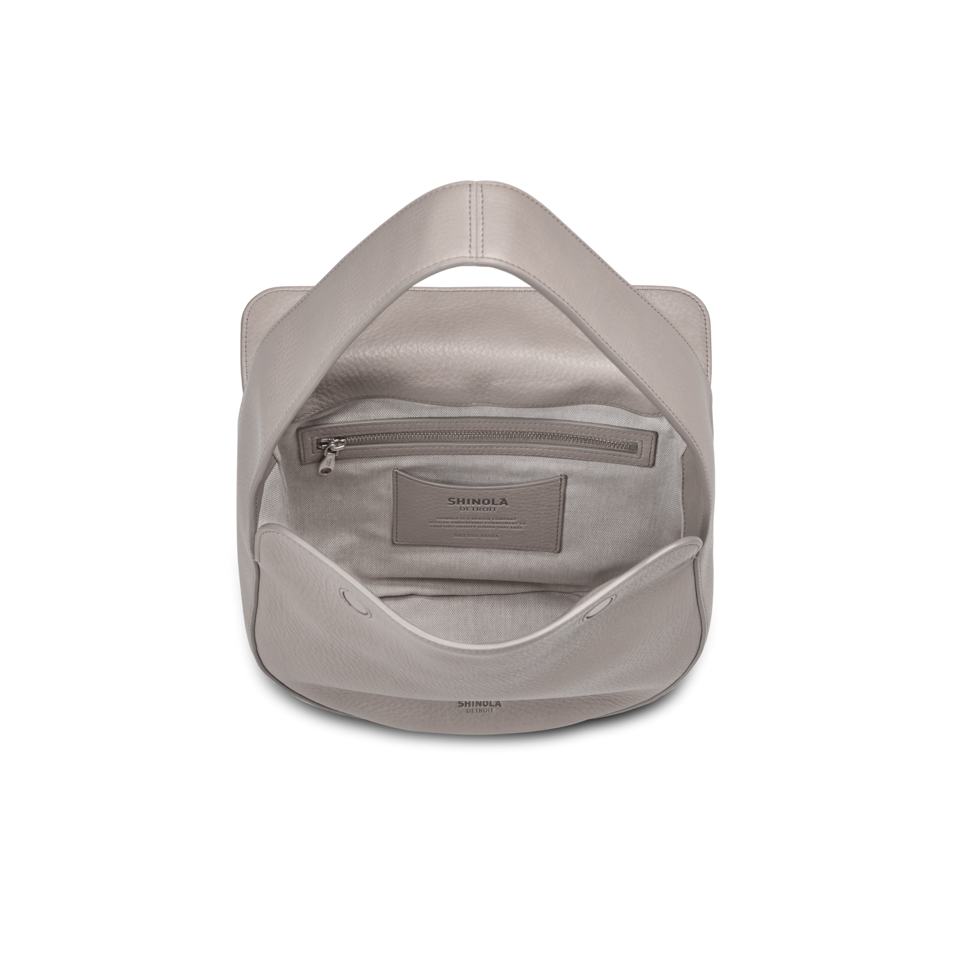 A top-down view of an open Shinola Small Shoulder Bag - Taupe in natural grain leather, revealing the interior with a zippered pocket and slip pocket, both displaying SHINOLA branding.