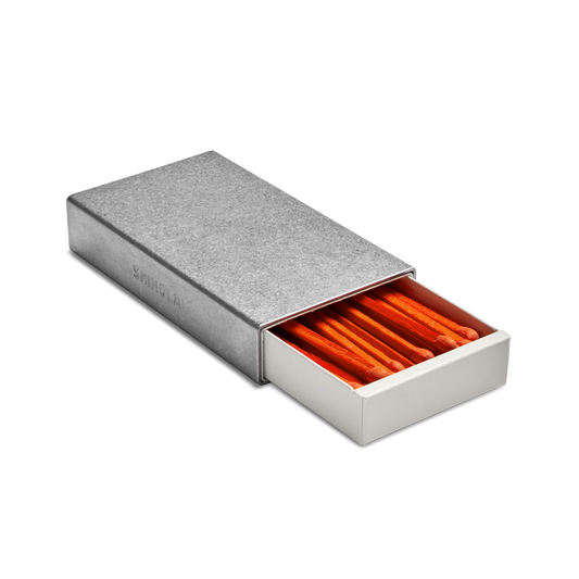 The Shinola Aluminum Matchbox Set features a rectangular, engravable case with a sliding drawer partially open to display neatly arranged orange-tipped matches inside.