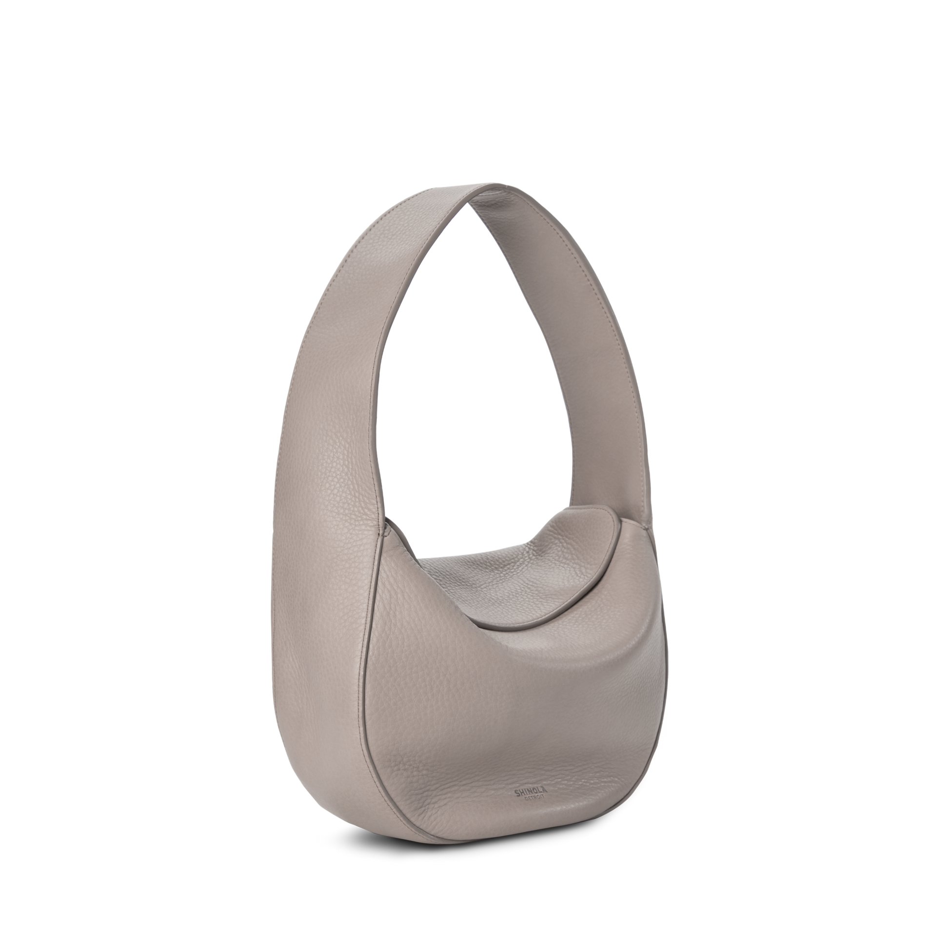 The Shinola Small Shoulder Bag - Taupe is a crescent-shaped bag made from natural grain leather, featuring a wide curved shoulder strap and minimalist style, shown against a plain white background.