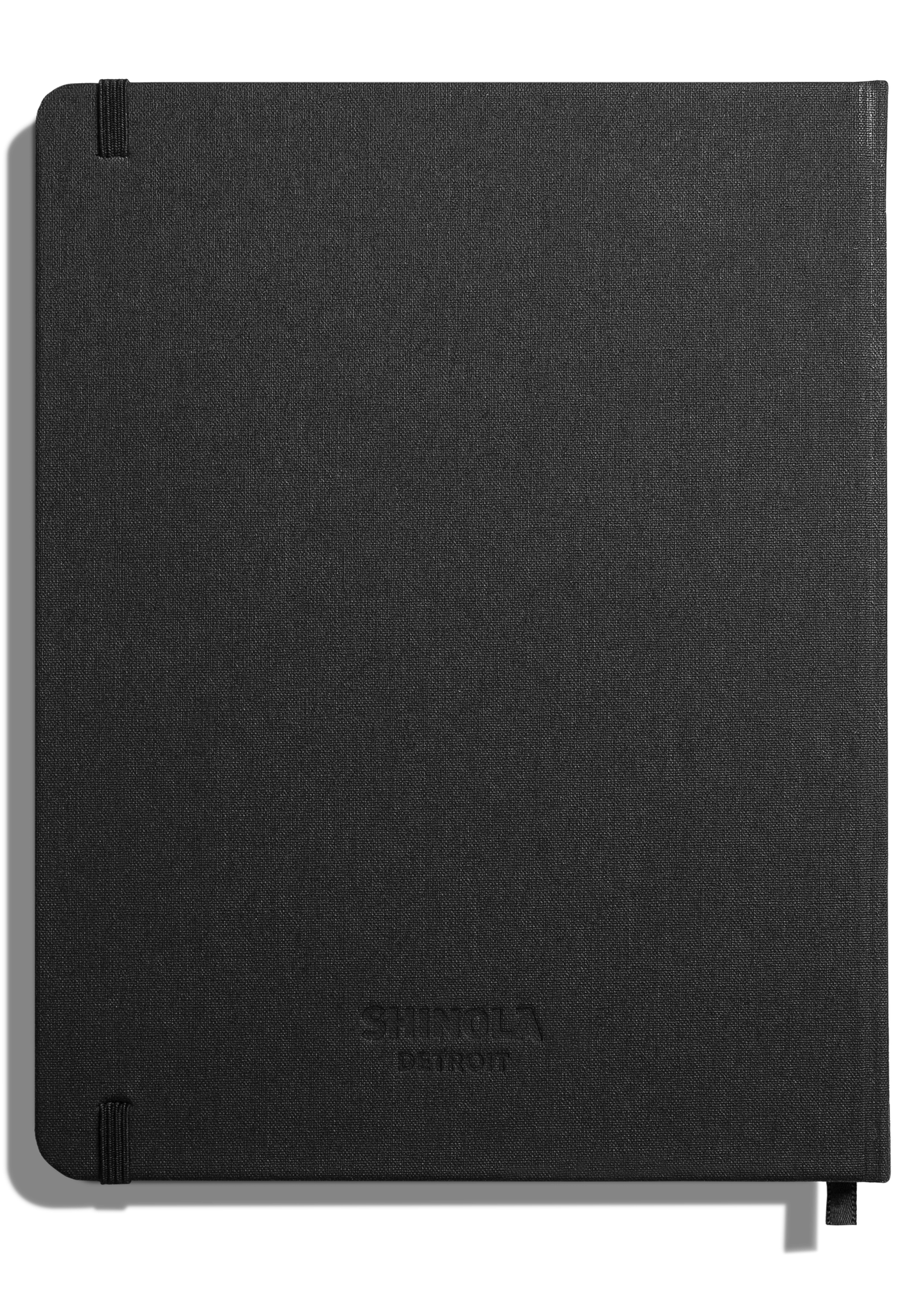 The Shinola Large Hard Ruled Journal in black features a fabric cover, rounded corners, acid-free pages, elastic closures on the top and bottom left, and a subtle Shinola logo embossed on the front.