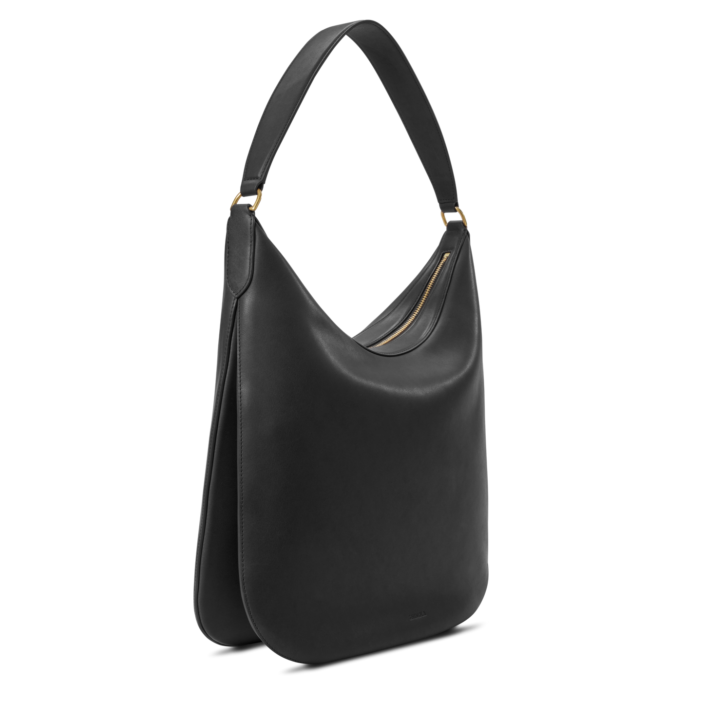 The Shinola Bixby Shoulder Bag - Black is crafted from natural leather with a single wide strap, gold hardware, and minimalist accordion-style construction, shown against a white background.