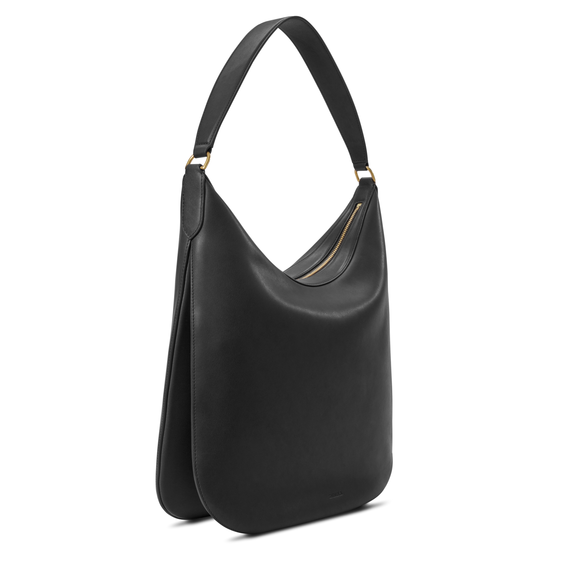 The Shinola Bixby Shoulder Bag - Black is crafted from natural leather with a single wide strap, gold hardware, and minimalist accordion-style construction, shown against a white background.