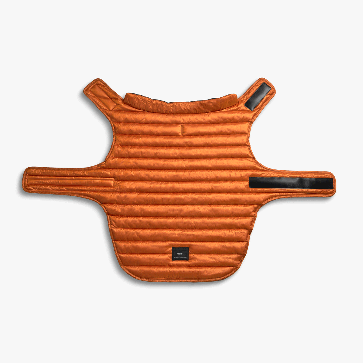 The Shinola Reversible Puffer Dog Coat in orange/black features padded warmth, horizontal stitching, adjustable Velcro straps at the neck and chest, and a small black label near the hem, shown laid flat on a white background.