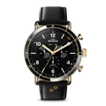 The Shinola Canfield Sport Watch - Dominos features a black and gold chronograph face with three sub-dials, a date window, white hour markers, two gold pushers, and is finished with a black leather strap. It also displays the day and month.