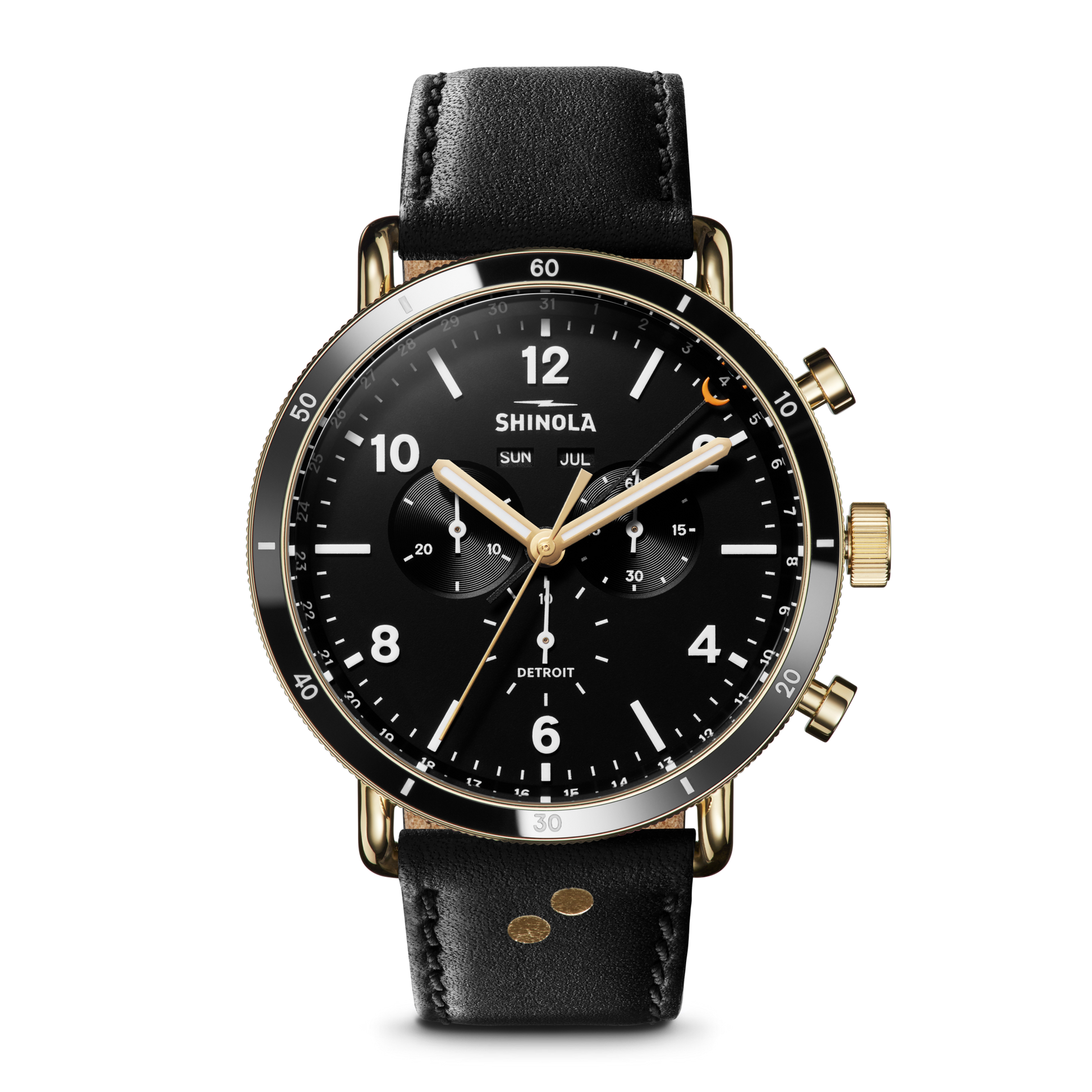The Shinola Canfield Sport Watch - Dominos features a black and gold chronograph face with three sub-dials, a date window, white hour markers, two gold pushers, and is finished with a black leather strap. It also displays the day and month.