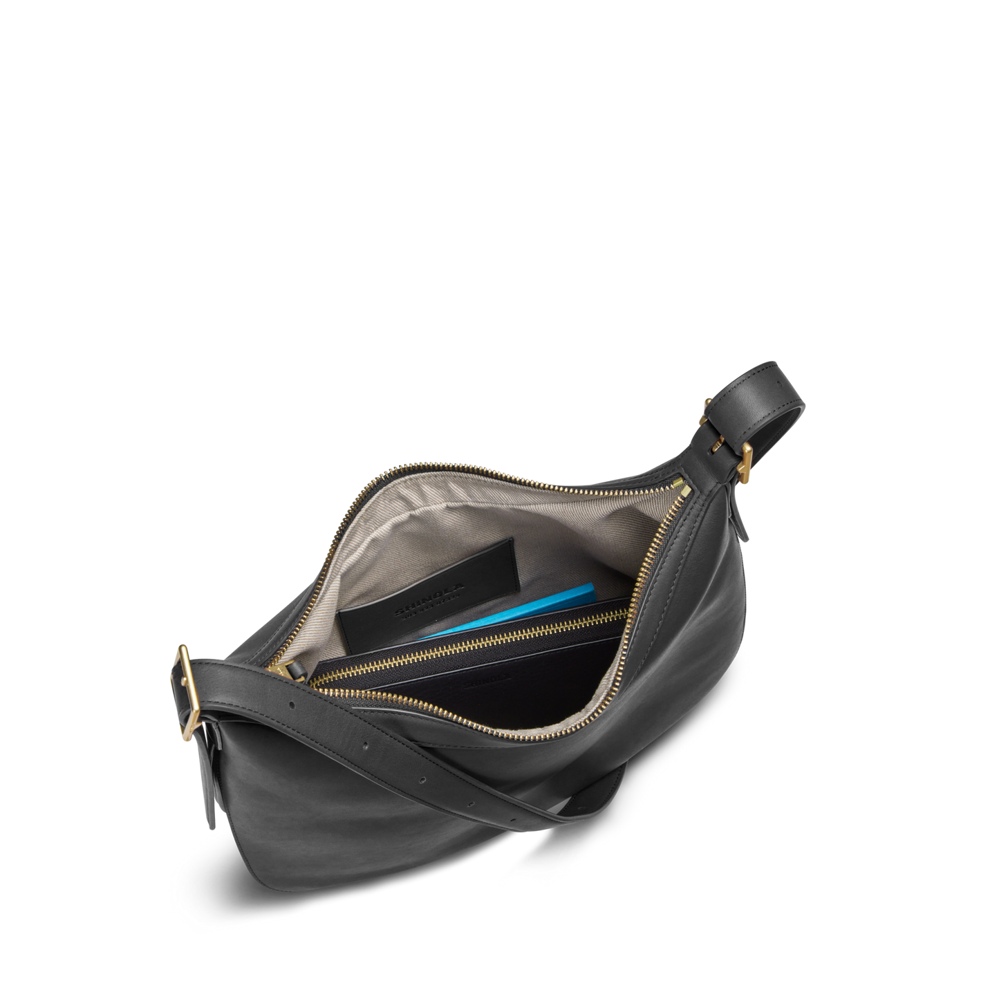 The Shinola Bixby Shoulder Bag - Black features natural leather, accordion-style construction, gold zipper, beige interior with zip pocket, room for a tablet or blue notebook, and an adjustable strap with gold buckle.