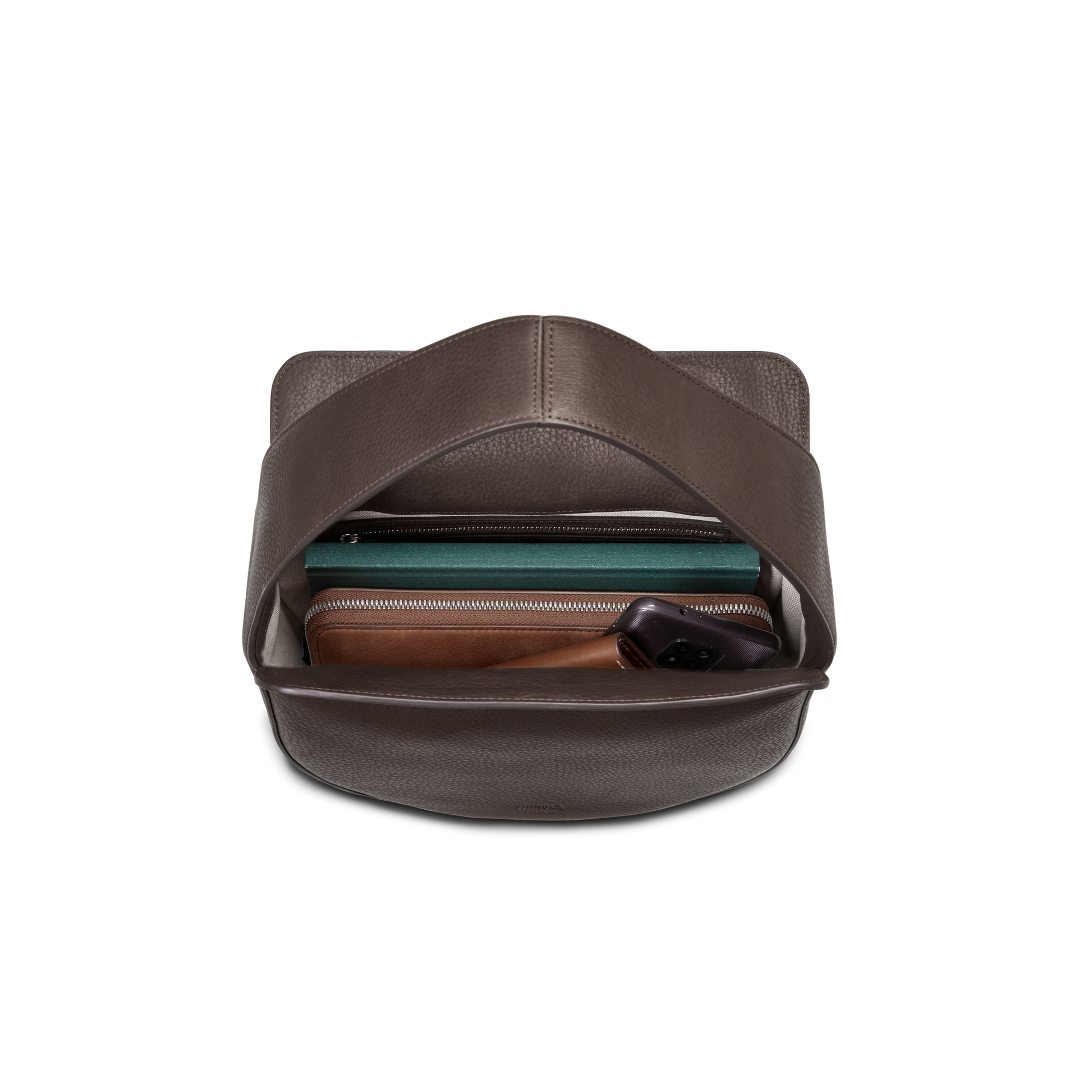 The Shinola Small Shoulder Bag - Espresso, made from natural grain leather with an open top, showcases premium craftsmanship and reveals a zippered green compartment, a brown wallet, and black wireless earbuds against a white background.