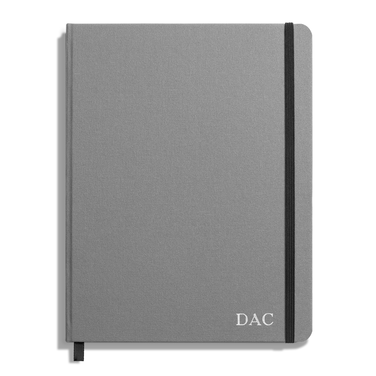 A closed Shinola Large Hard Ruled Journal in stone gray linen with a black elastic band on the right edge and the initials DAC printed in white on the bottom right corner of the cover.