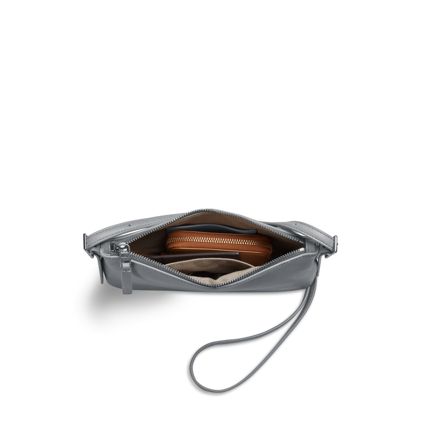 The Shinola Small Bixby Crossbody in Mist, crafted from natural leather with a zipper closure, is shown partially open to reveal a brown zippered pouch and other essentials—an ideal everyday accessory against a white background.