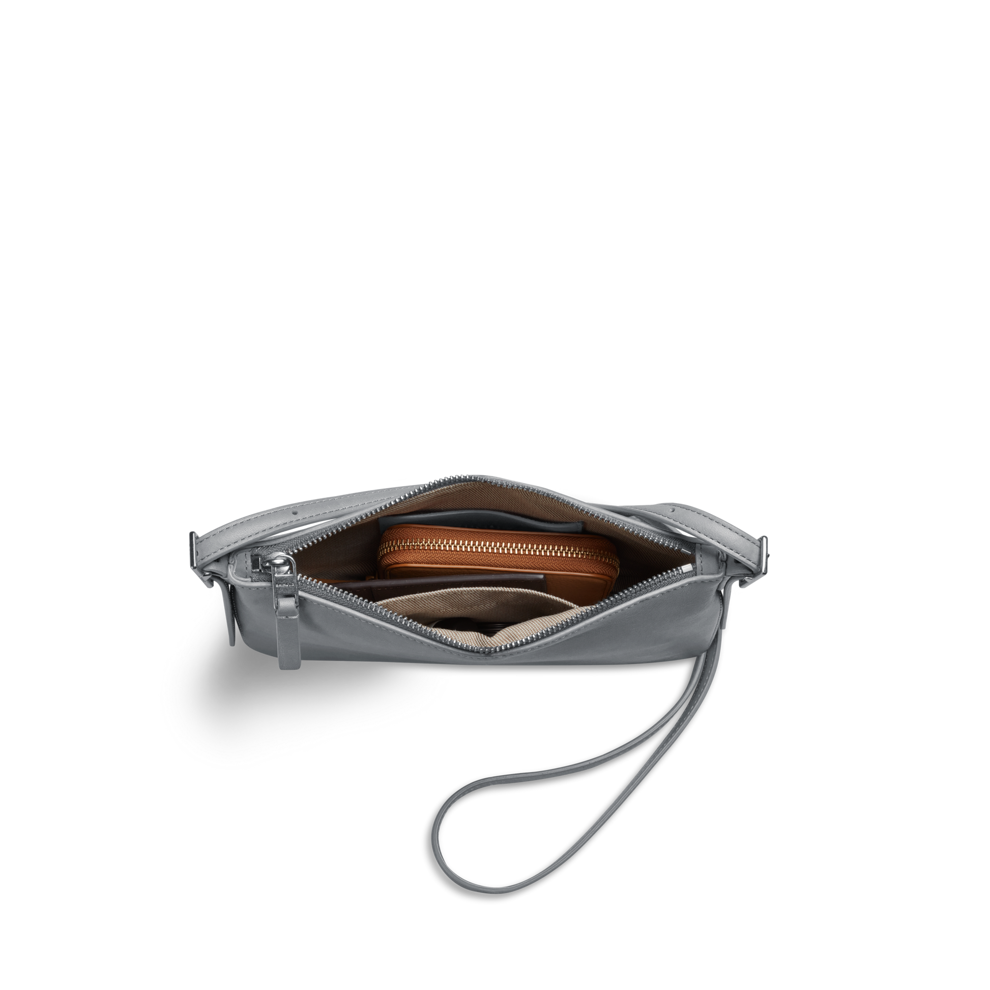 The Shinola Small Bixby Crossbody in Mist, crafted from natural leather with a zipper closure, is shown partially open to reveal a brown zippered pouch and other essentials—an ideal everyday accessory against a white background.
