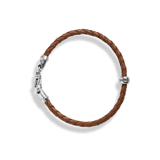 The Shinola Single Wrap Woven Leather Bracelet in tan features a sterling silver clasp and an engraved silver bead, shown on a white background.