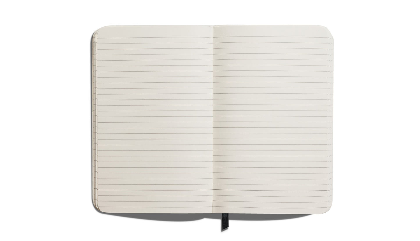 A Shinola Medium Hard Ruled Journal in Cobalt, featuring acid-free lined pages and a black ribbon bookmark, is shown open from above on a white background.
